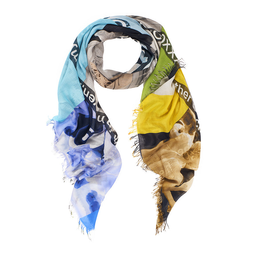 The SUZI ROHER "Cheek To Cheek" scarf is a lightweight, colorful silk piece with frayed edges and an abstract blue, yellow, green, and neutral design, partial white text, and a tribute to Fred Astaire’s Top Hat style.