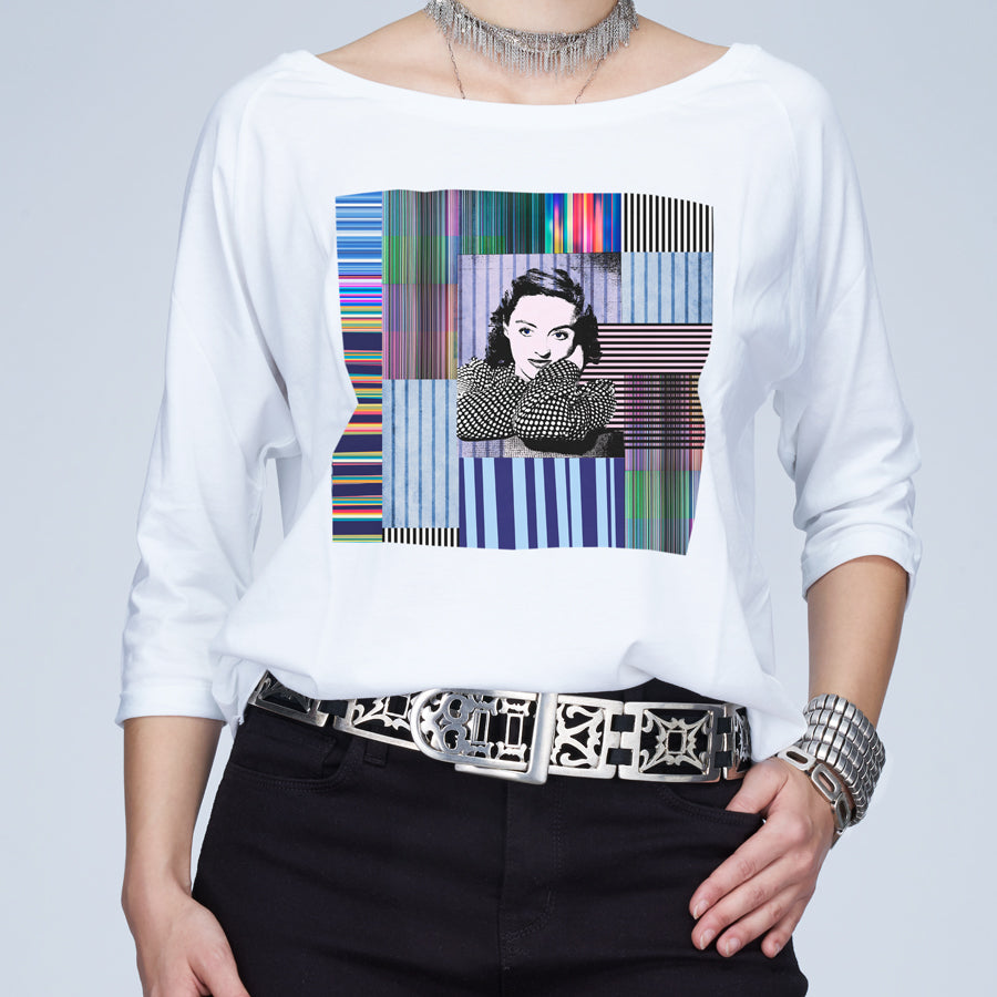 Wearing The Bailey by SUZI ROHER—a boxy cut tee with a colorful geometric Bette Davis and woman’s portrait graphic—styled with a metallic belt, chunky bracelet, and silver choker necklace. Their face is partially out of frame.