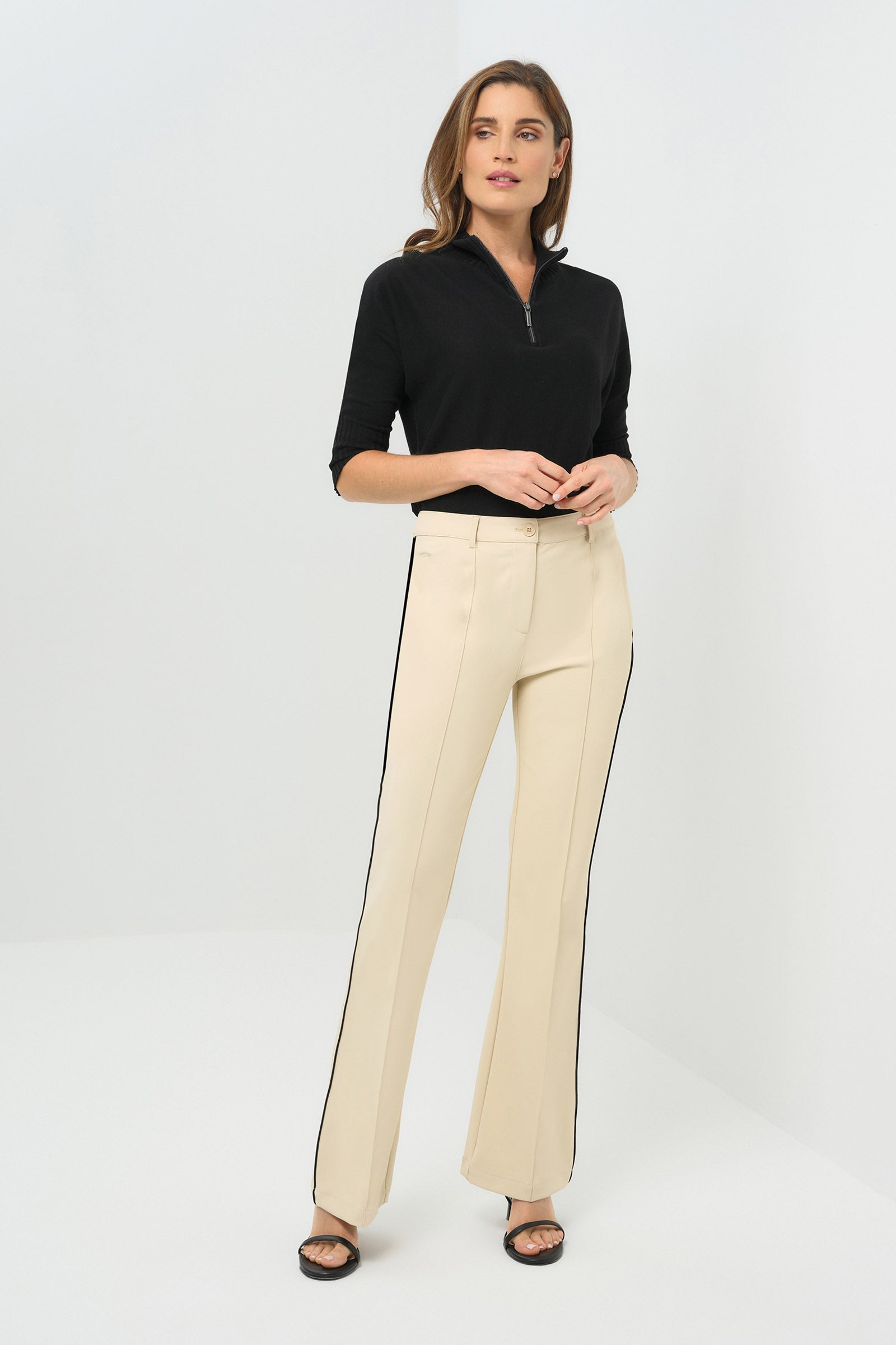 Front view of wheat pants with a black stripe on the side, paired with a black quarter-zip knit top featuring a high collar.