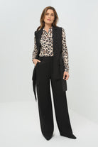 Front view cheetah-print button-down blouse layered under a long black sleeveless vest with flap pockets and a tie detail. Paired with high-waisted, wide-leg black cargo trousers.
