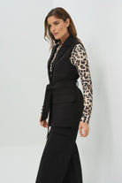 Side view of a black vest tied at the waist, paired with a cheetah-print button-up shirt and slim black pants.