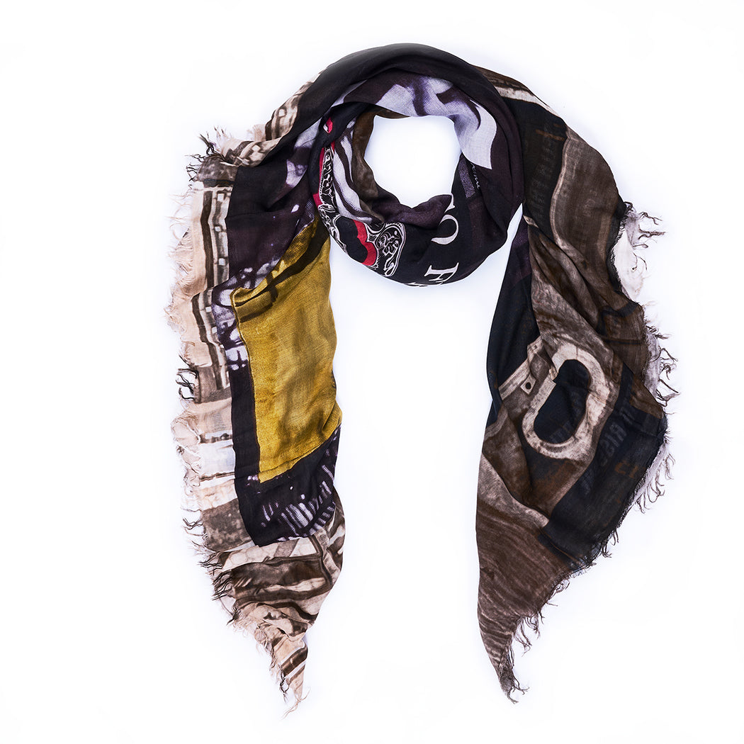 The SUZI ROHER "8 1/2" scarf features a loose coil with frayed edges and showcases abstract patterns in dark brown, black, yellow, and beige, presented against a white background.