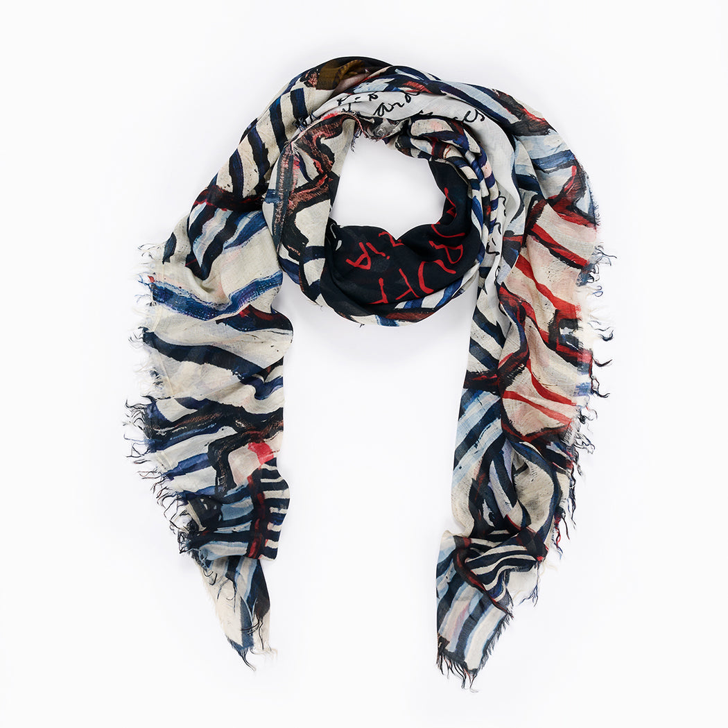 The SUZI ROHER "Dubuffet" is a rectangular scarf with frayed edges, displaying an abstract pattern in black, white, blue, and red—loosely arranged in a circle on a white background.