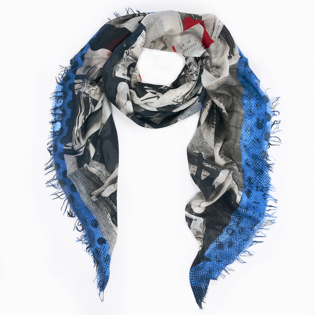 The L'Espresso scarf by SUZI ROHER is a triangular piece with fringed edges, showcasing a black-and-white photo collage inspired by the iconic Italian magazine and a bold blue border. Arranged in a loose loop with hanging ends. Made in Italy.