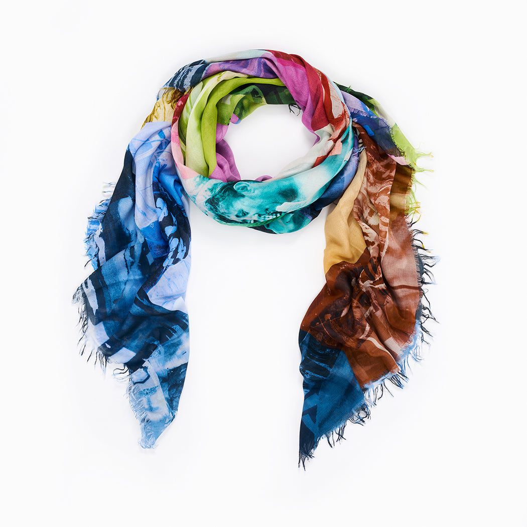 The "Life Is A Beach" scarf by SUZI ROHER is a lightweight modal silk piece made in Italy, featuring frayed edges and a vibrant abstract pattern in blue, green, pink, brown, and yellow. It's displayed in a loose loop on a white background.