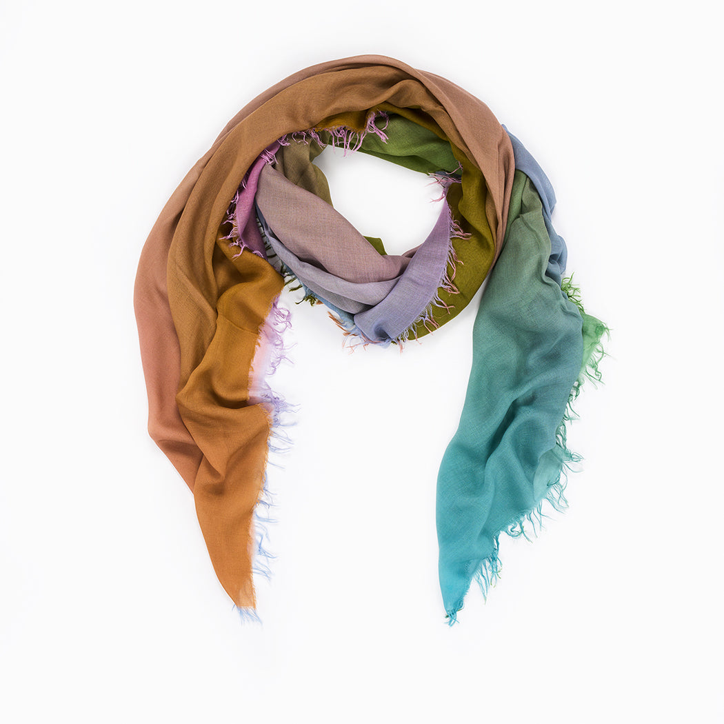 The SUZI ROHER Morning Has Broken v.02 is an Italian-made, lightweight modal silk scarf with frayed edges, showcasing a cloud of brown, pink, green, and blue shifting in a loose spiral on a white background.
