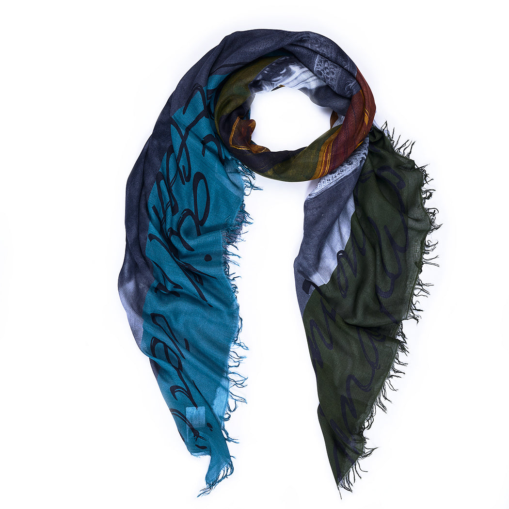 The SUZI ROHER "Red Heart" scarf, adorned with fringed edges and bold script, features sections of teal, green, blue, and brown. It is displayed in a loose loop against a white background.