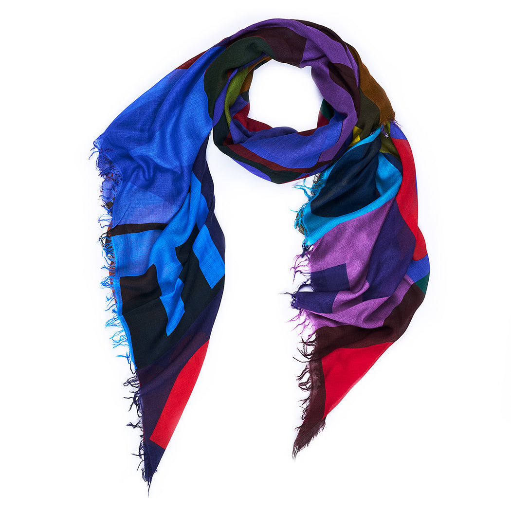 The SUZI ROHER TRUE scarf features colorful geometric patterns in purple, blue, red, and green tones with frayed edges, loosely rolled into a loop against a white background.