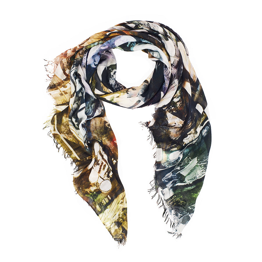 The Cottage by SUZI ROHER is a silk scarf with frayed edges, arranged in a loose spiral on a white background. Made in Italy, it features an abstract pattern in green, yellow, blue, and brown.