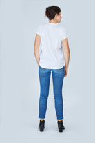 Exuding timeless elegance, this woman poses against a light gray backdrop in SUZI ROHER's The Viv—a white t-shirt styled with blue jeans and black ankle boots—her hair neatly tied back, capturing classic Silver Screen charm.