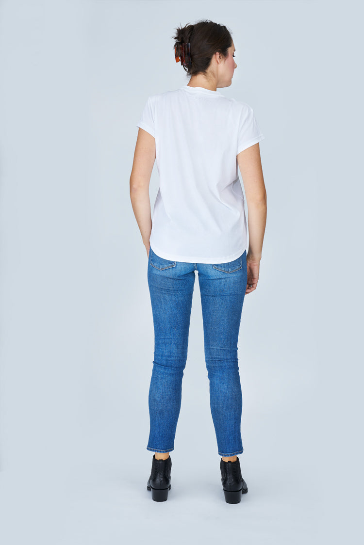 Exuding timeless elegance, this woman poses against a light gray backdrop in SUZI ROHER's The Viv—a white t-shirt styled with blue jeans and black ankle boots—her hair neatly tied back, capturing classic Silver Screen charm.