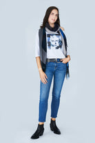 A woman with shoulder-length dark hair wears SUZI ROHER's The Bailey, a boxy-cut 3/4 sleeve tee, styled with blue jeans, black ankle boots, a black belt, and a black-and-white portrait print scarf. She stands facing forward with one hand in her pocket.