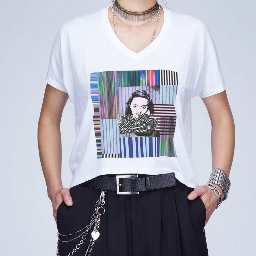 Model wears The Velvet tee by SUZI ROHER, a white boxy cut top with a vibrant geometric and striped graphic of a thoughtful illustrated woman, styled with layered necklaces, bracelets, and black belted pants.