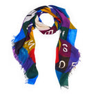The SUZI ROHER "Sweet Love" scarf features a geometric patchwork in blue, yellow, red, green, and purple with scattered white letters and frayed edges, shown loosely looped on a white background.