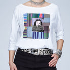 Wearing The Bailey by SUZI ROHER—a boxy cut tee with a colorful geometric Bette Davis and woman’s portrait graphic—styled with a metallic belt, chunky bracelet, and silver choker necklace. Their face is partially out of frame.
