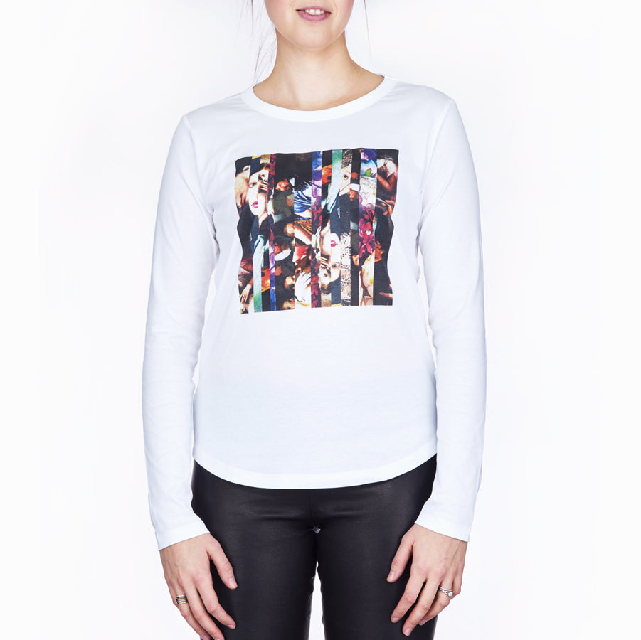 A woman wearing SUZI ROHER's "The Catherine"—a long-sleeve white shirt featuring a colorful, Renaissance-inspired abstract graphic—paired with black pants, stands against a plain white background. Her face is partially out of frame.