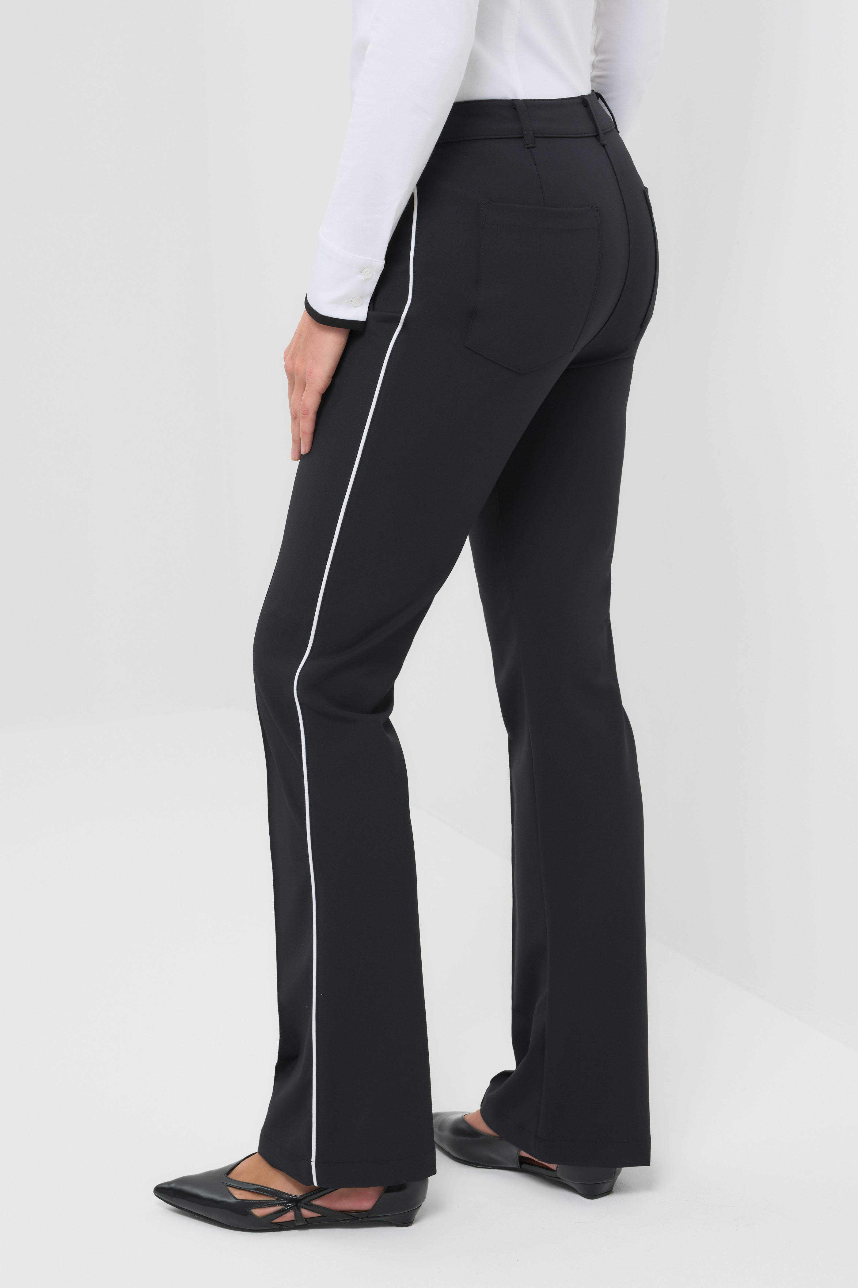 Side view black high-waisted tailored pants featuring a slim fit through the thigh and a subtle flare at the hem. Designed with clean front seams and accented by contrast side stripes for a modern, elongating effect.