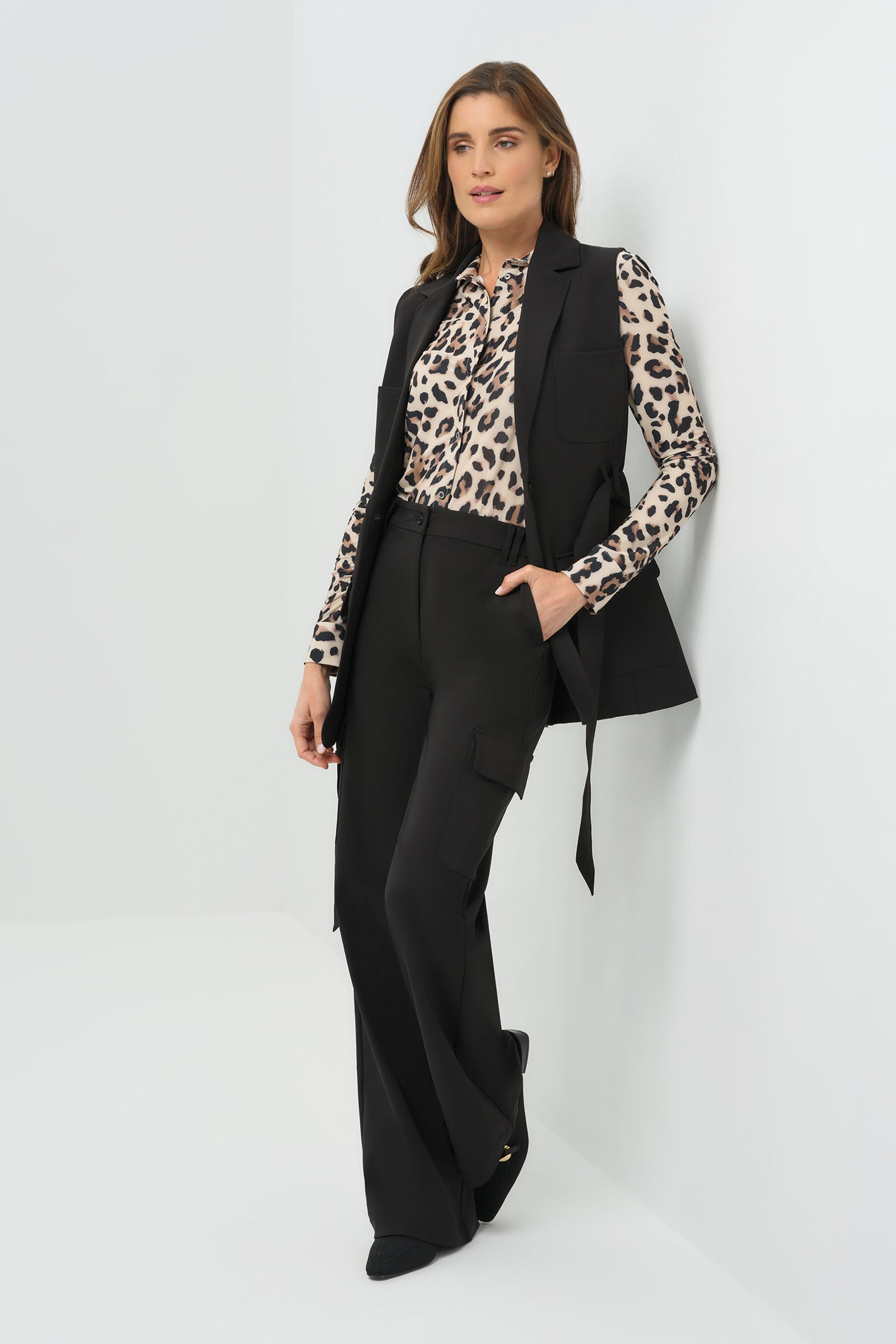 Woman wearing a black vest, leopard print shirt, and black pants on a white background