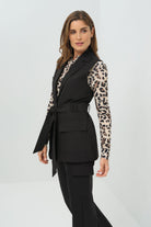 Side view of a black vest tied at the waist, paired with a cheetah-print button-up shirt and slim black pants.