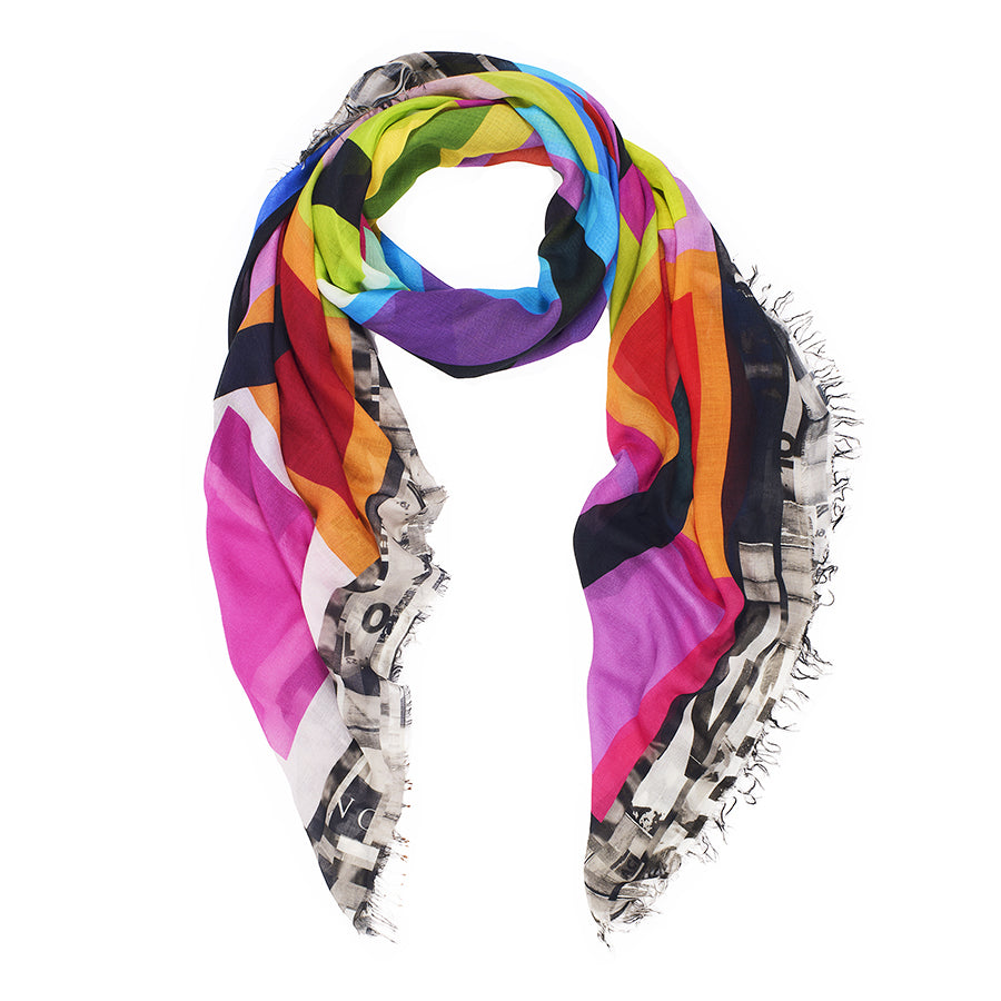 The SUZI ROHER Cozy scarf features vibrant diagonal stripes in pink, purple, blue, green, yellow, orange, and black on modal silk blanket fabric with frayed edges and a black-and-white graphic print at one end.