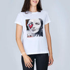 A woman with shoulder-length brown hair wears The Niki by SUZI ROHER—a classic 100% cotton white tee featuring a black-and-white portrait of a woman's face with a red heart painted over one eye.