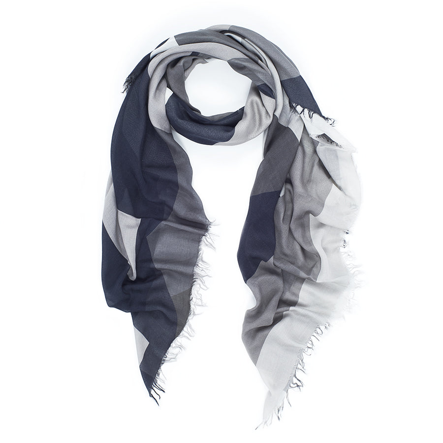 The SUZI ROHER "Electric Love- B&W" scarf features a loosely coiled geometric pattern in dark blue, gray, and white with fringe edges, inspired by BØRNS’ “Electric Love,” and is displayed on a white background.