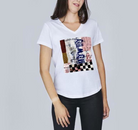 A woman wears The Viv by SUZI ROHER—a white cotton V-neck tee with colorful abstract designs—paired with black pants, standing against a plain gray background.