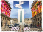 In a city square with colorful abstract art and a tall monument, people cross the pink “CROSS WALK” wearing the SUZI ROHER Kim Cross Walk soft modal silk blanket under fluffy clouds.