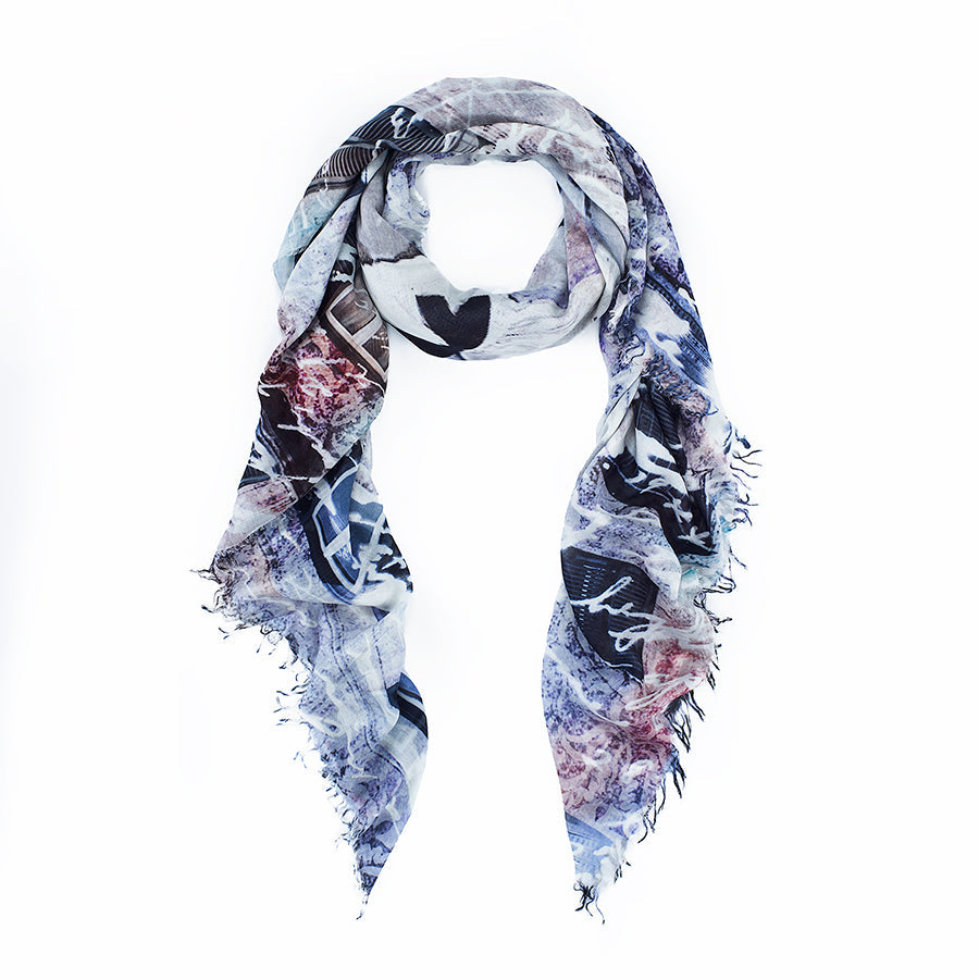 The Notorious Landlady scarf by SUZI ROHER is a lightweight, rectangular accessory with frayed edges and an abstract blue, purple, gray, and white pattern—timelessly elegant against a plain white background.