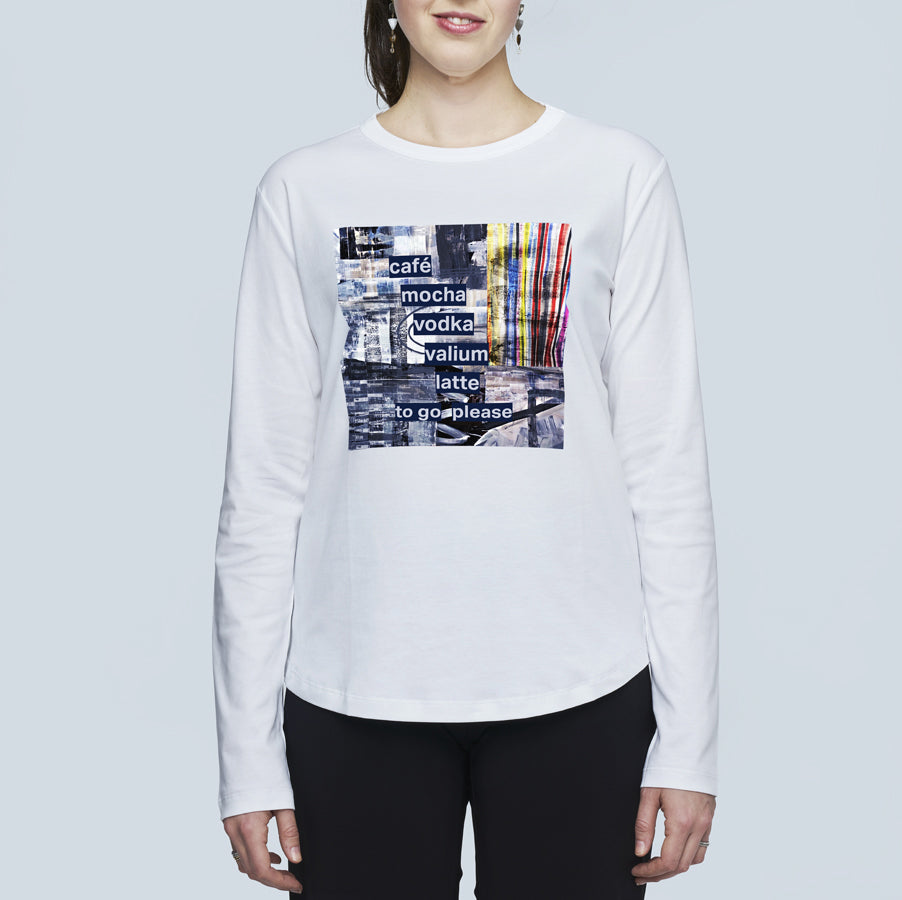 A woman stands against a light background wearing The Catherine by SUZI ROHER, a slim-fit cotton tee with a colorful graphic and "café mocha vodka valium latte to go please" printed on the front.