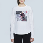A person wears The Catherine by SUZI ROHER—a white long-sleeve shirt with an abstract female samurai graphic, bold text, and artistic elements—while standing against a light gray background.