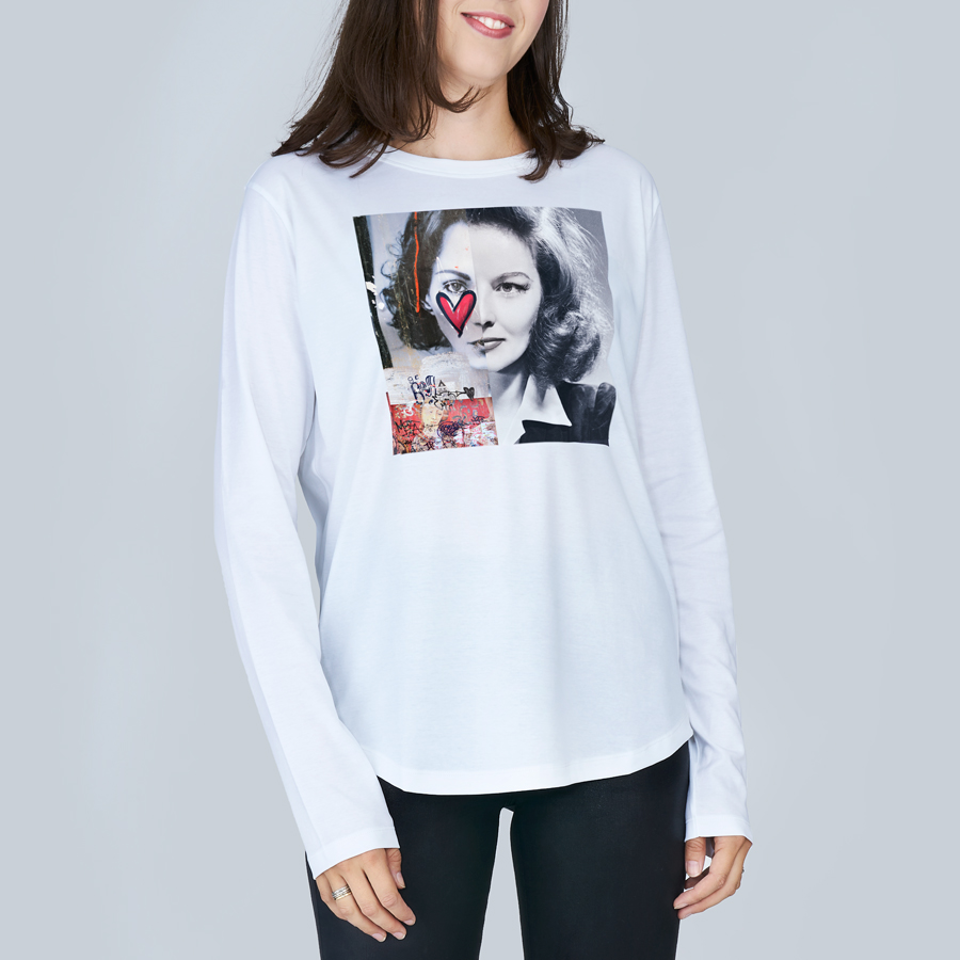 A woman wears The Catherine long-sleeve slim-fit crew neck tee by SUZI ROHER—100% cotton with a black-and-white graphic of a woman's face, red heart accent, and colorful details—paired with black pants.
