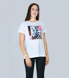 A woman with long brown hair models SUZI ROHER's "The Niki" white graphic t-shirt, inspired by Frank Sinatra's "My Way," paired with black skinny jeans against a light gray background.