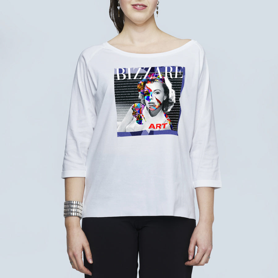 A woman wears The Bailey by SUZI ROHER—a white, oversized boxy tee with three-quarter sleeves and a vibrant BIZZARE ART collage on the front—styled with black pants and a silver bracelet.