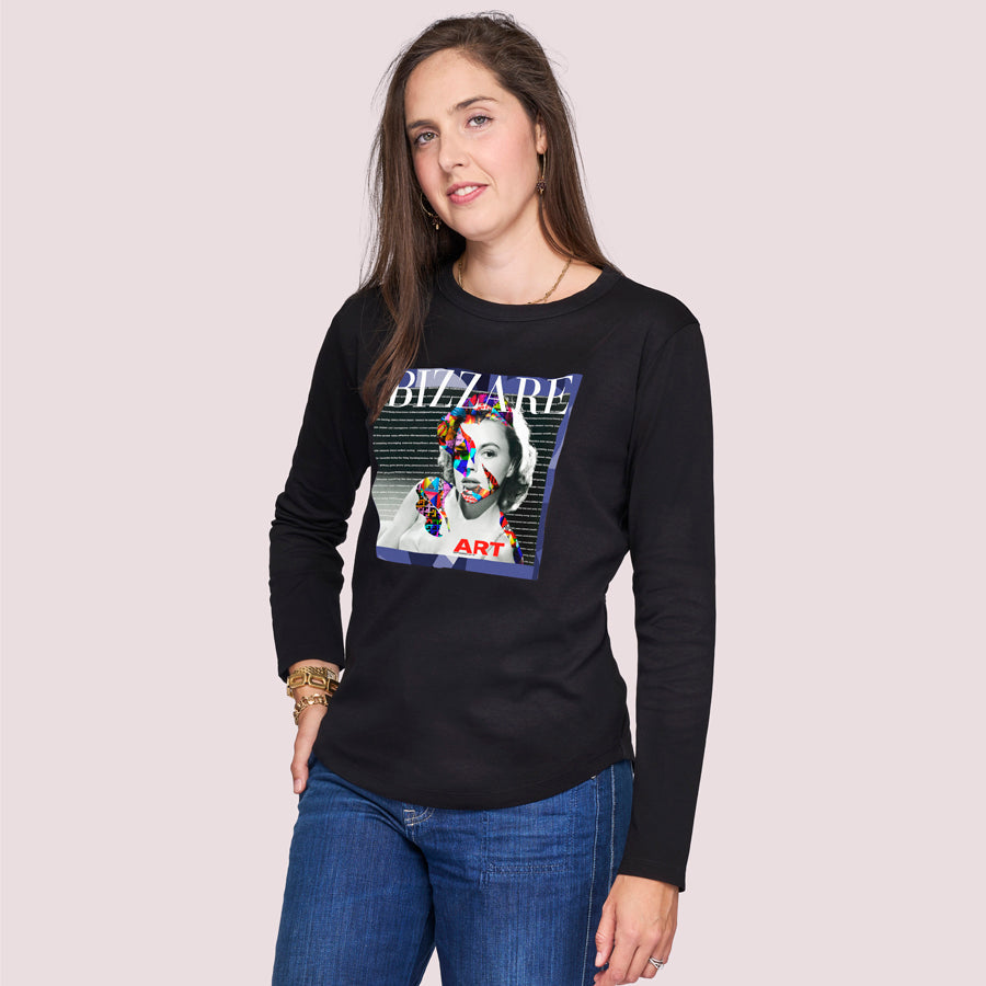 A woman with long brown hair models The Catherine by SUZI ROHER, a black 100% cotton crew neck shirt with colorful abstract art and “BIZZARE” on the front, set against a plain light background.