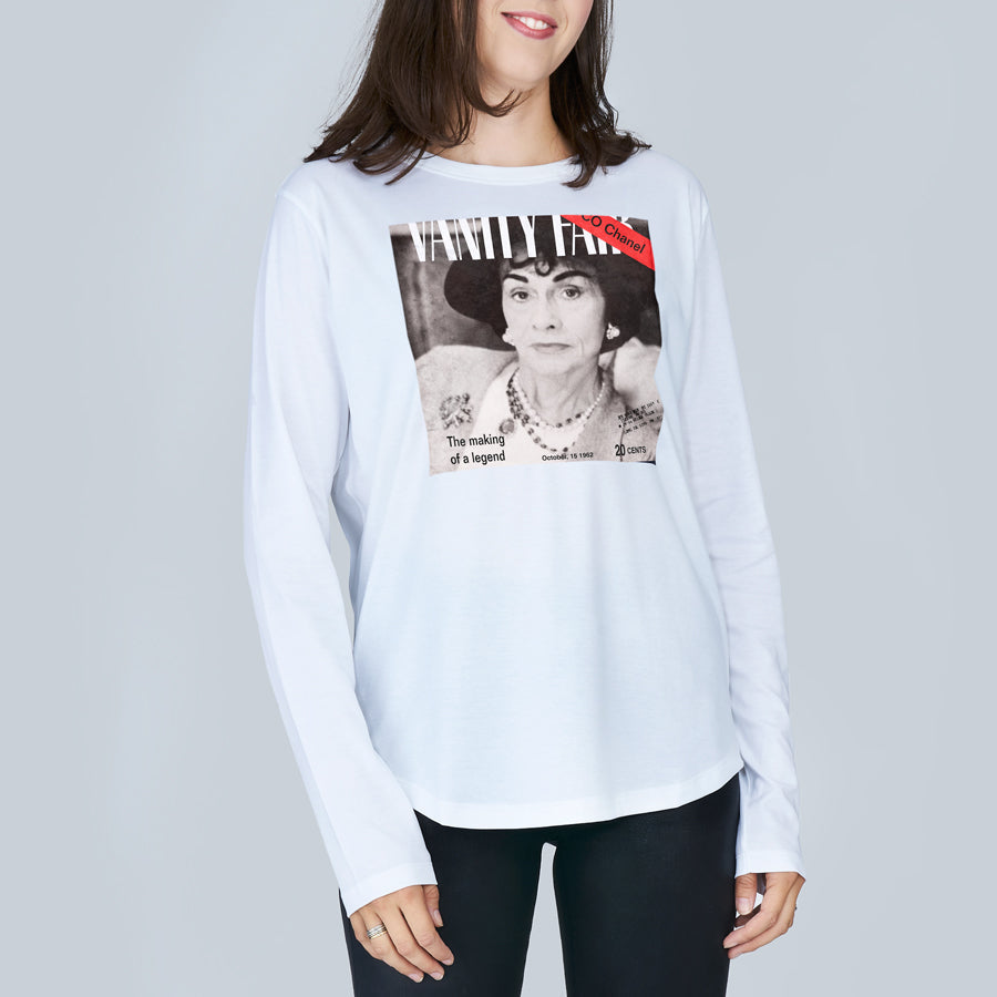 A woman wears The Catherine by SUZI ROHER, a slim-fit white long-sleeve shirt featuring a black-and-white Vanity Fair cover print with a woman in pearls and a hat, plus the text "The making of a legend.