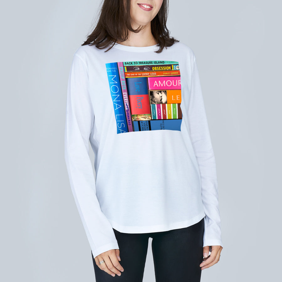 A woman wears The Catherine by SUZI ROHER, a clean-cut 100% cotton tee featuring a colorful graphic of vertically stacked books—Amour, Mona Lisa, and Back to Treasure Island—on the front.