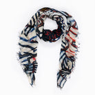 The SUZI ROHER "Dubuffet" is a rectangular scarf with frayed edges, displaying an abstract pattern in black, white, blue, and red—loosely arranged in a circle on a white background.