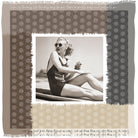 A vintage-style photo features a woman in a swimsuit and sunglasses, holding a drink on a beach towel. Beside her is the Ginger silk scarf by SUZI ROHER, bordered with a patterned frame and handwritten cursive text along the edges.