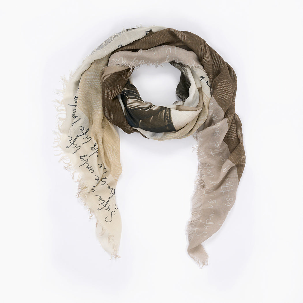 The SUZI ROHER "Ginger" scarf features light and dark brown silk with frayed edges, faint handwritten-style white text, and a loosely draped design that channels effortless elegance.