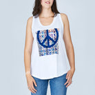 A woman wears The Lola tank top by SUZI ROHER—100% cotton, white with a blue peace symbol and blue patterned front—paired with blue jeans, standing against a light gray background.