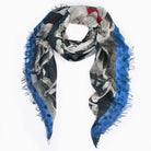 The L'Espresso scarf by SUZI ROHER is a triangular piece with fringed edges, showcasing a black-and-white photo collage inspired by the iconic Italian magazine and a bold blue border. Arranged in a loose loop with hanging ends. Made in Italy.