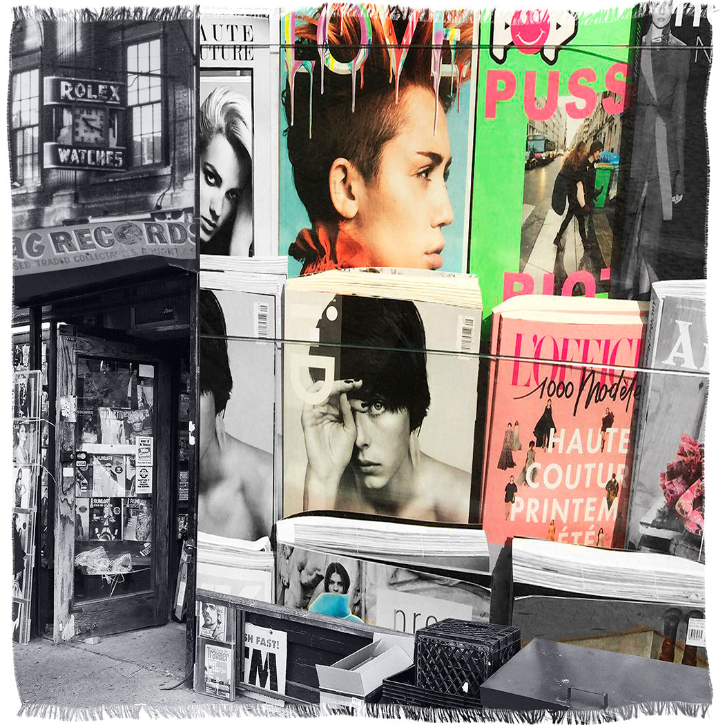 A street newsstand displays colorful SUZI ROHER "L'Officiel" French fashion magazines featuring model faces and luxury Modal Silk, contrasting with a black-and-white storefront covered in posters and signs.
