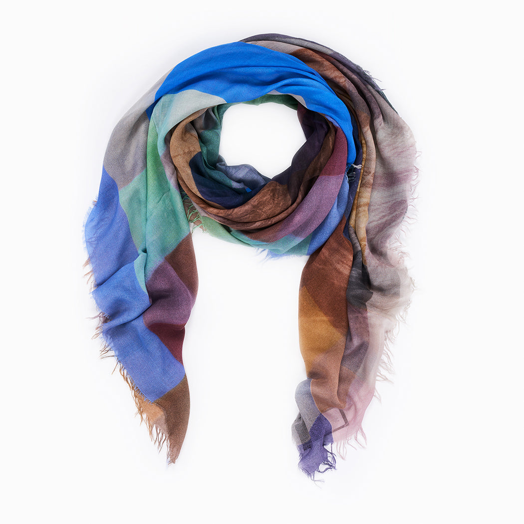 The Lennie scarf by SUZI ROHER, crafted from lightweight modal silk with a vibrant abstract pattern in blue, brown, purple, and green, is loosely rolled on a white background—perfect for expressing "Give Peace a Chance.