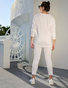 A creative woman wearing The Victoria by SUZI ROHER and sunglasses stands near a white building and a round gate, inspiring others to Make Art Not War on a sunny day.